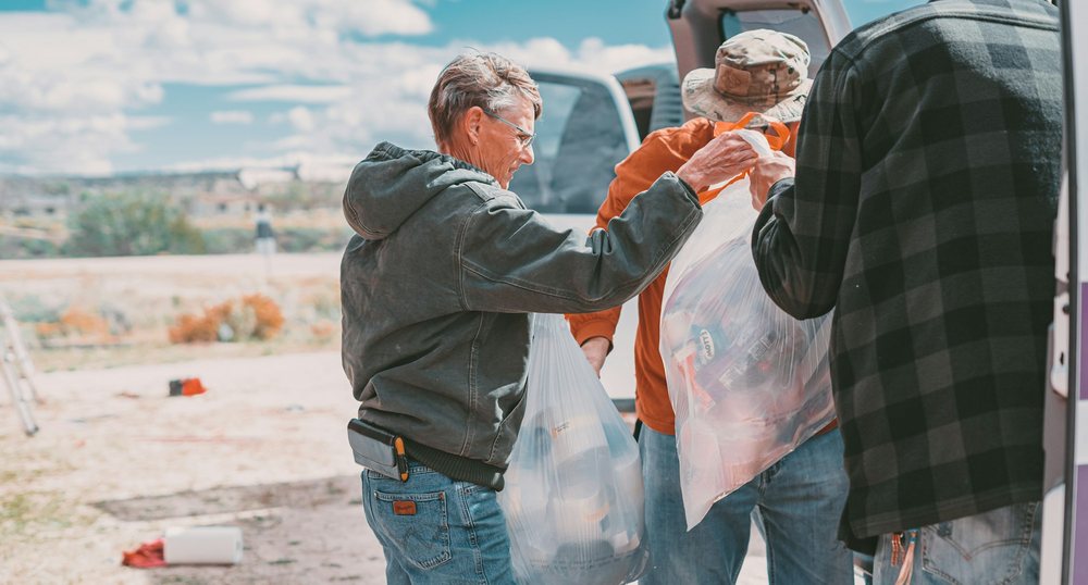 Neighbors hand bags of food and supplies to one another at the back of a truck.